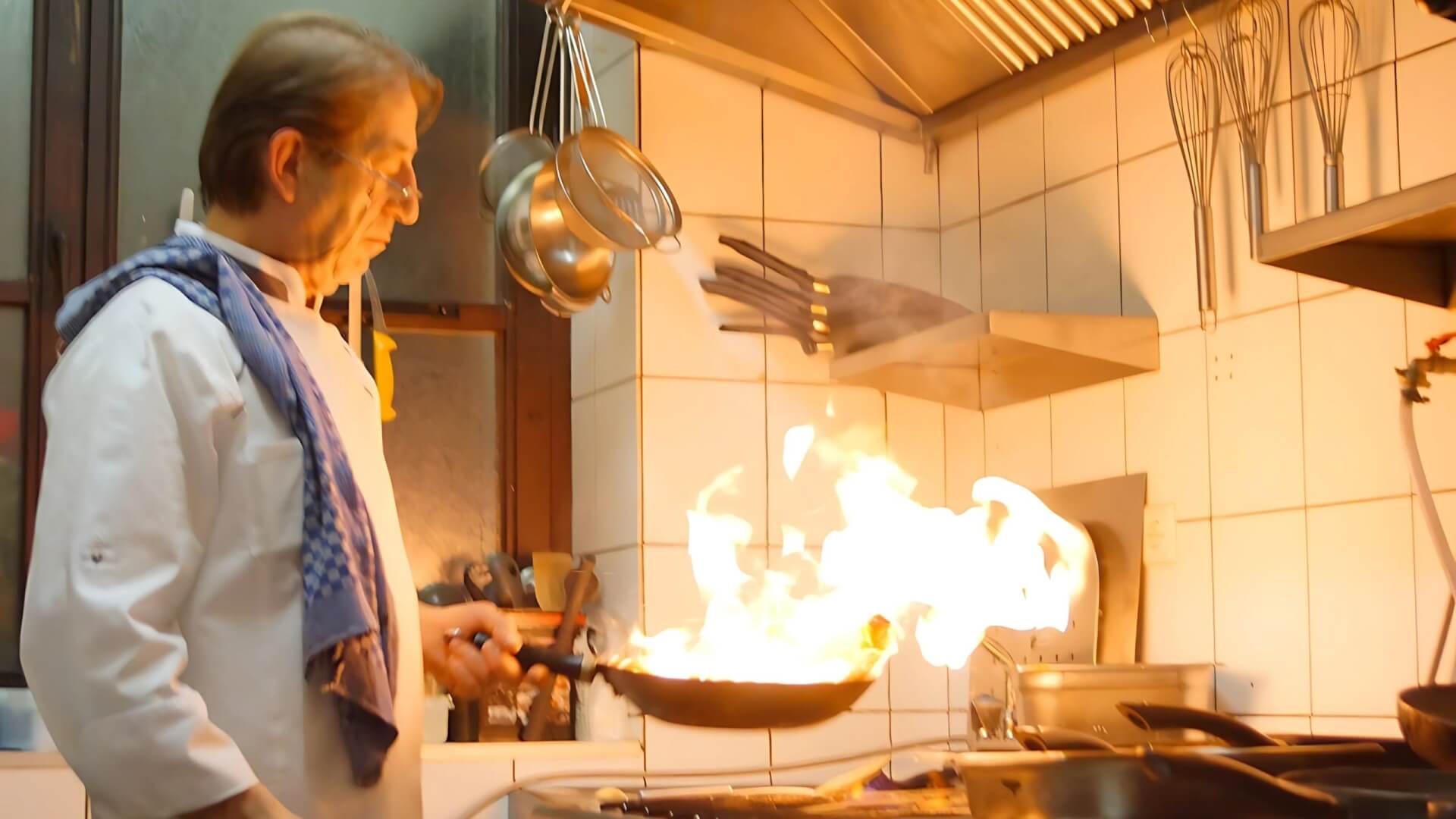 Küchenchef flambiert in der Restaurantküche, während im Gastraum ein Krimidinner läuft